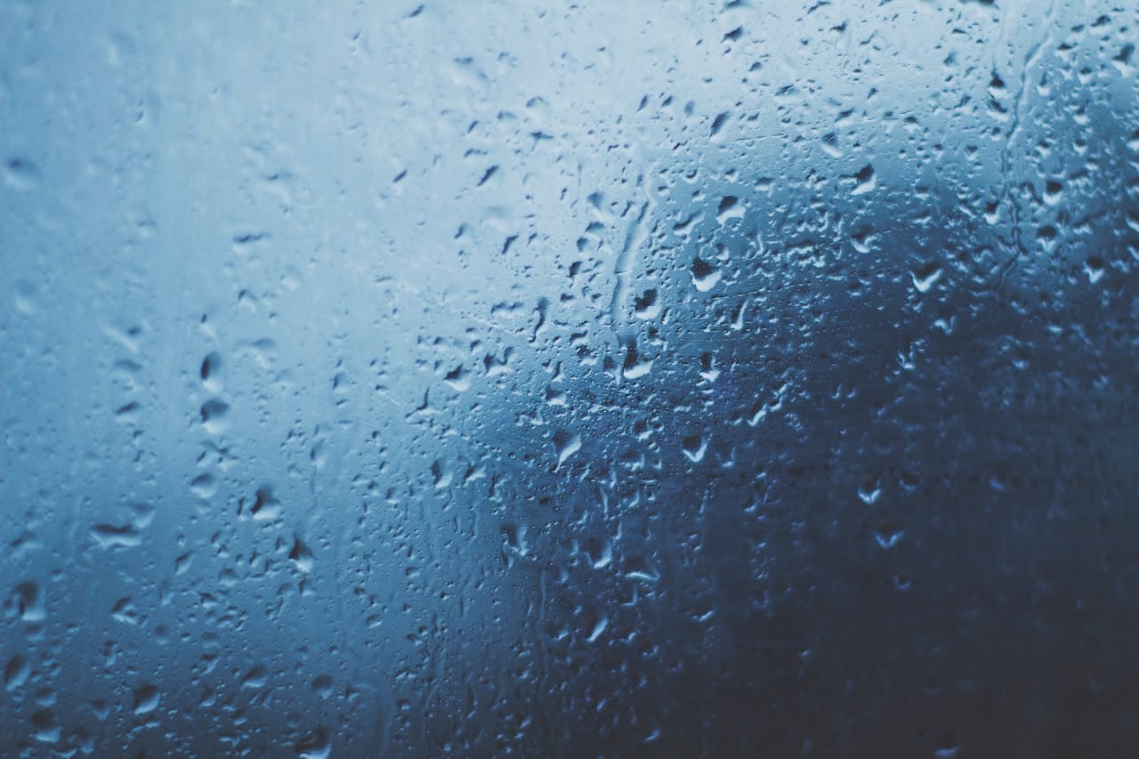 services-02 Detailed view of water droplets on a glass window with a blue background.