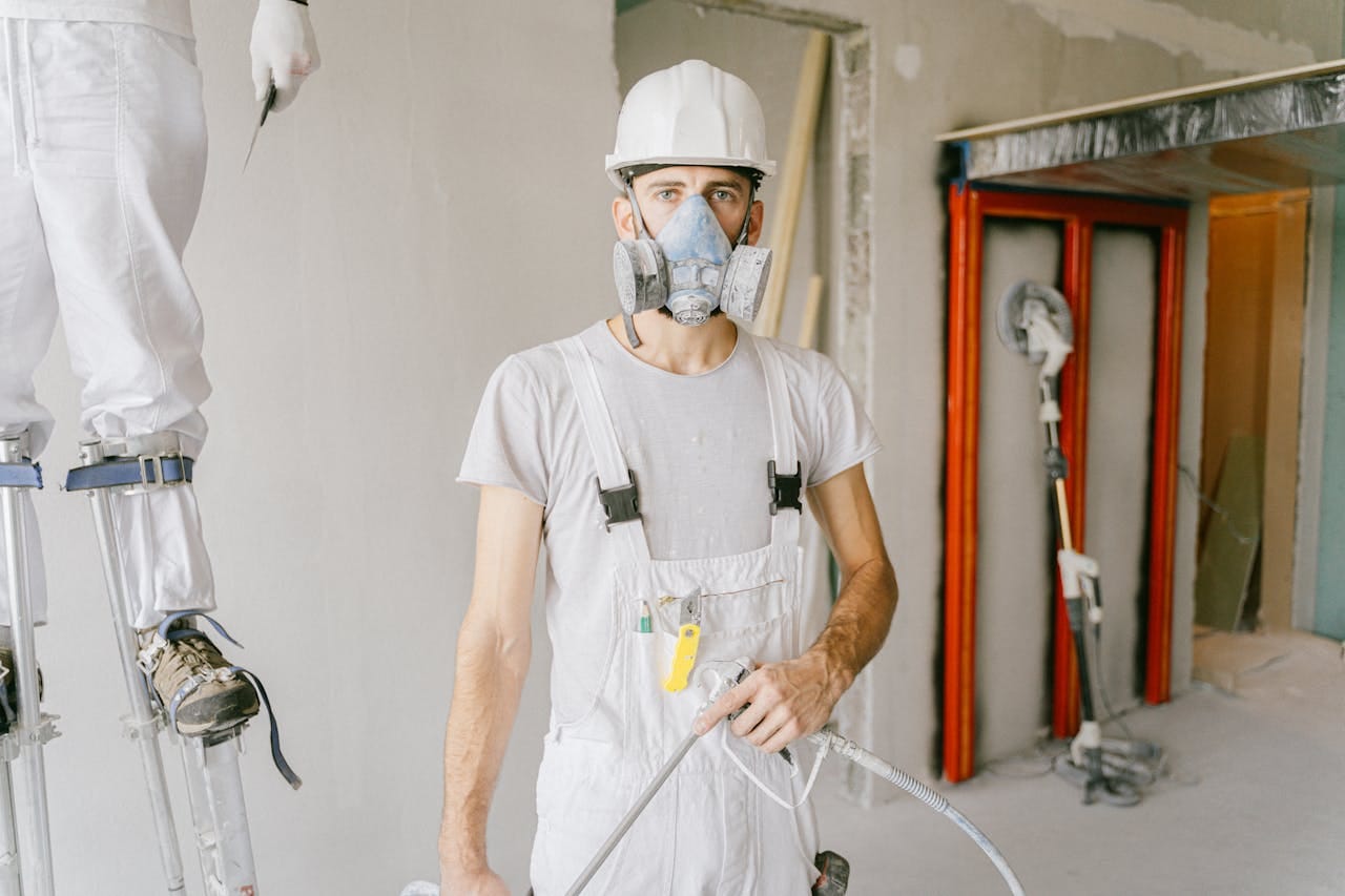 about-04 A construction worker wearing protective gear and prepping the wall during renovation indoors.