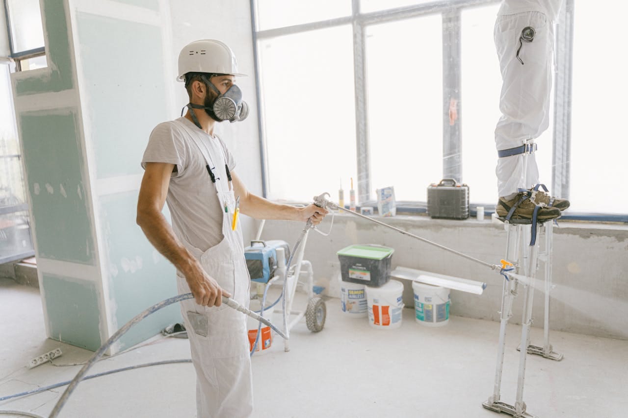 about-01 Two construction workers wearing protective gear and painting interior walls for a renovation project.