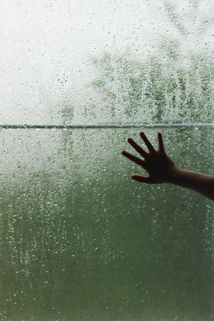 our-story-01 A hand touching a raindrop-covered window, creating a contemplative mood.